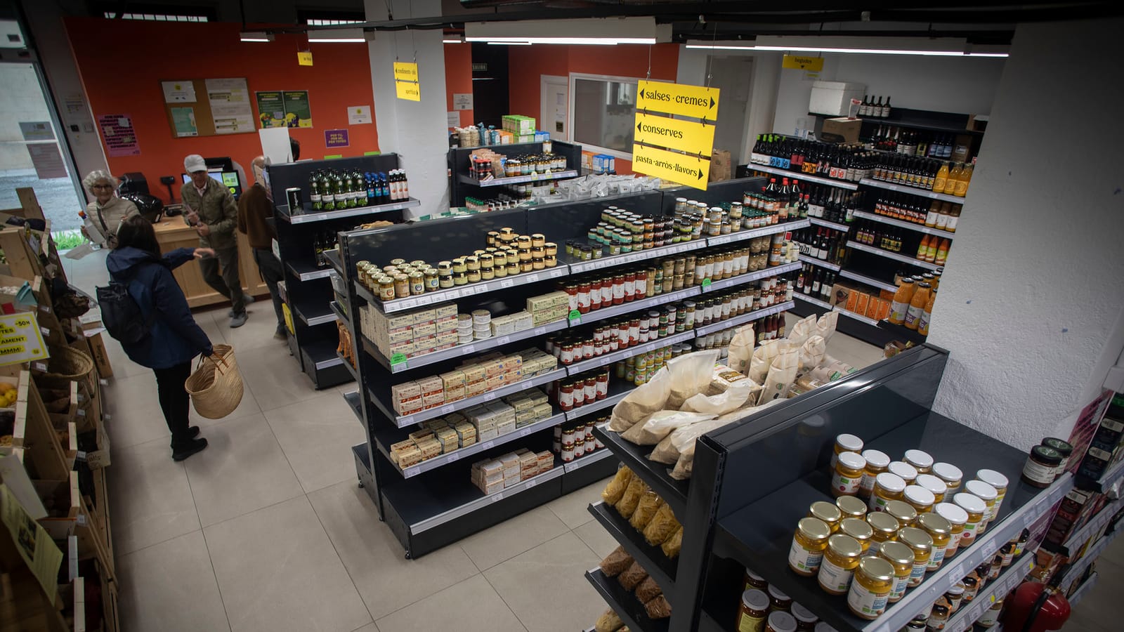Interior del súper amb els prestatges plens i unes quantes persones comprant.