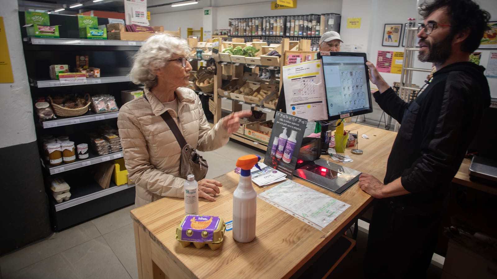 Una clienta paga la compra al taulell mentre una sòcia l’atén des de la caixa.