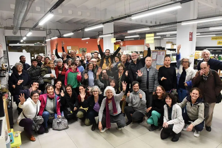 Un grup nombrós de persones posen somrients dins del súper, unes dretes i altres ajupides, i algunes amb els braços aixecats.