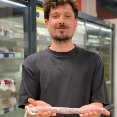 El Gerard, amb cabells arrissats, barba i samarreta negra, sosté un fuet llarg amb les dues mans davant les neveres del súper.